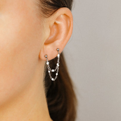 Silver double chain stud earring worn on two lobe piercings with white enamel beads