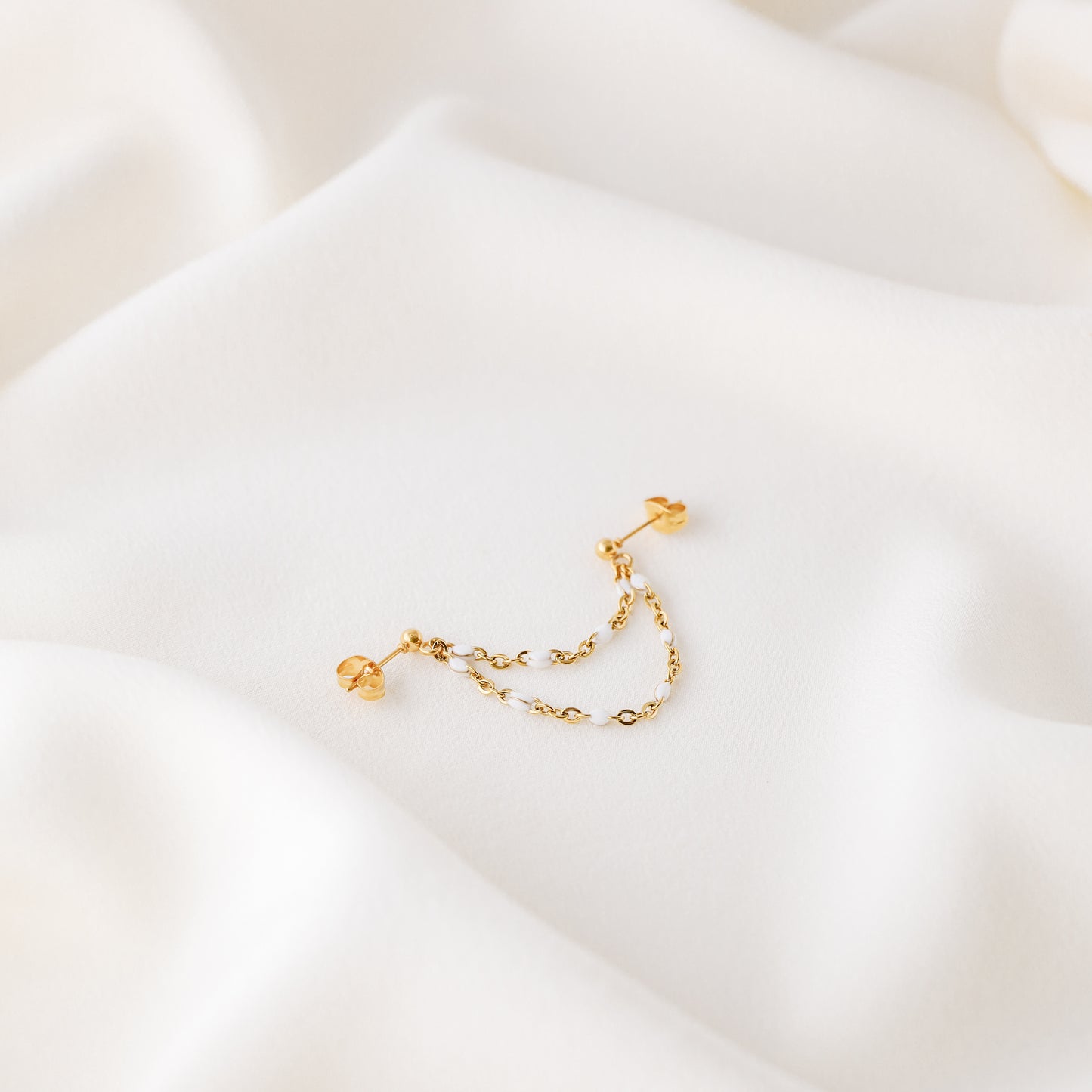 Gold double chain stud earring displayed on white fabric with delicate draped chains