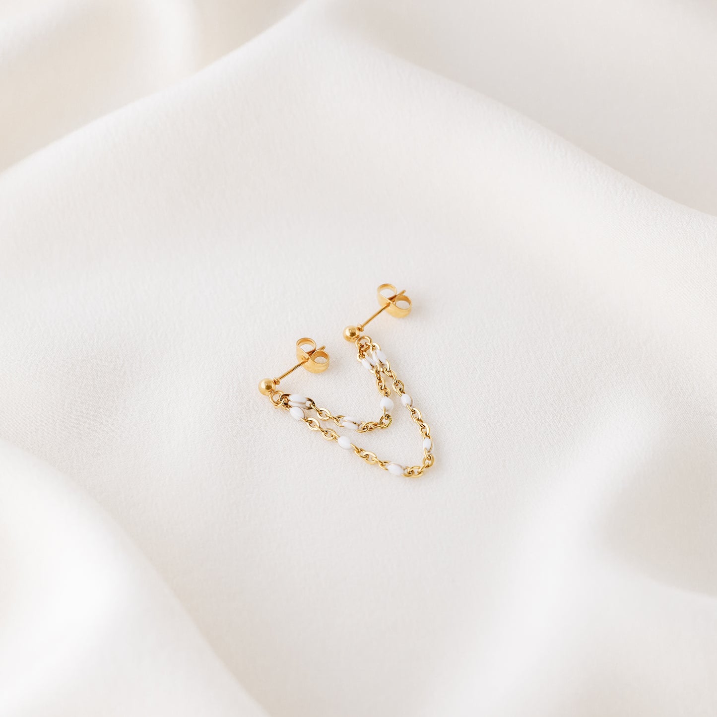 Gold double chain stud earring displayed on white fabric with delicate draped chains