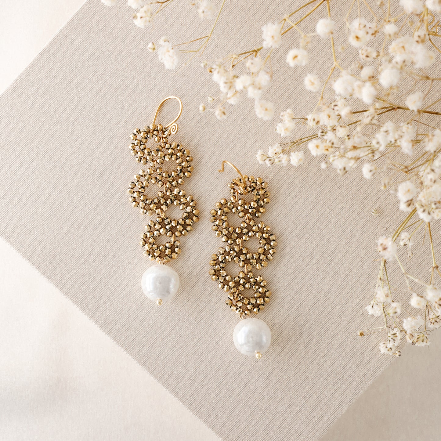 Gold crystal cascading earrings with pearl drop on neutral fabric background