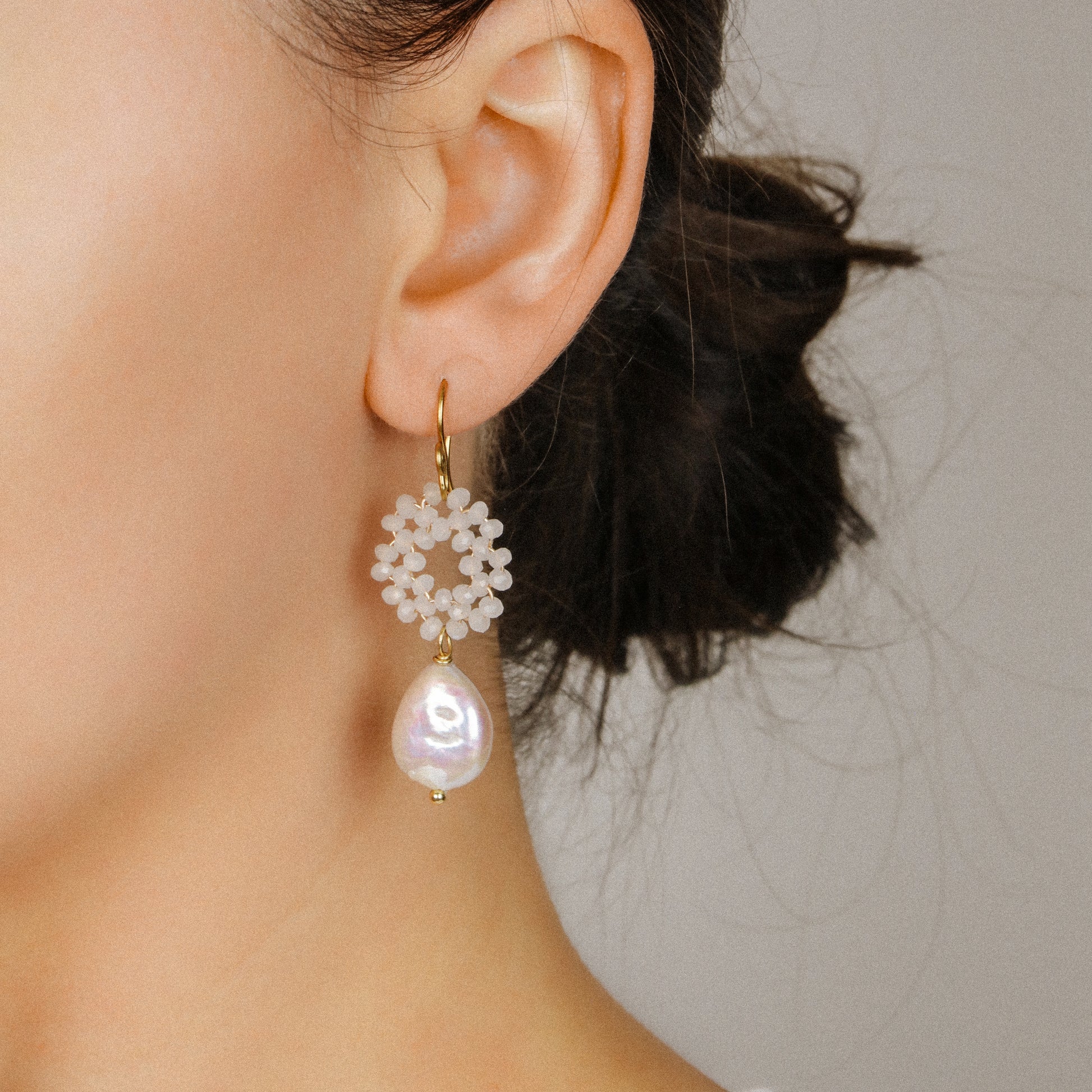 Close-up of a woman wearing a gold-plated baroque pearl drop earring with a delicate white crystal wreath, showcasing its elegant bohemian style.