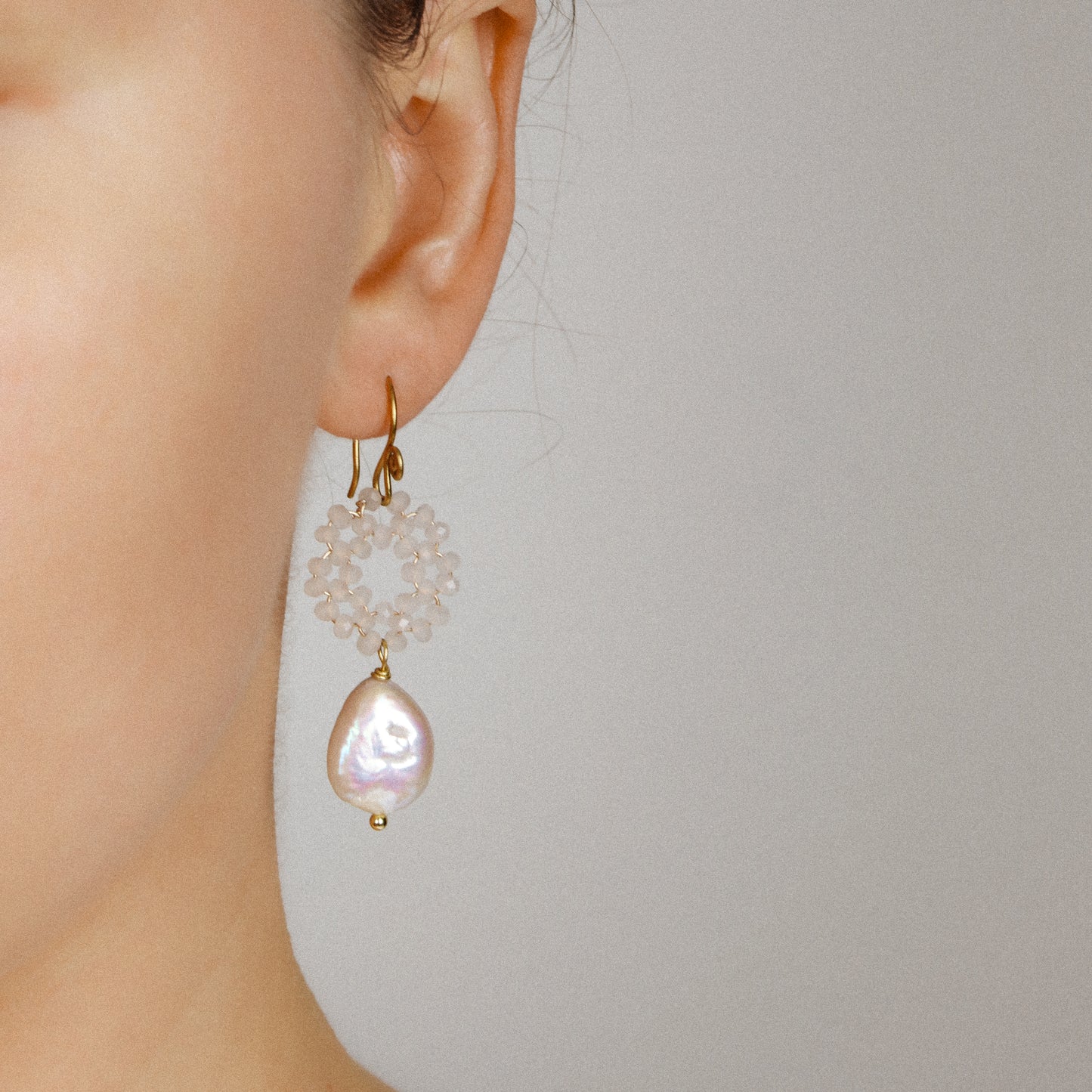 Close-up of a silver-toned baroque pearl drop earring worn on ear, featuring a sparkling circular wreath of faceted white glass beads.