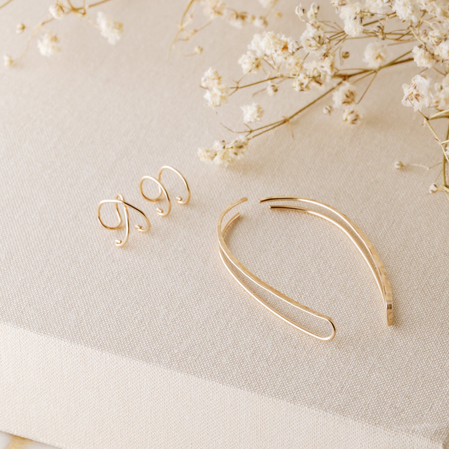 4 pieces ear climber set displayed on beige fabric with dried white flowers, featuring a pair of long hammered ear climbers, one Double Line no-piercing helix cuff and one Criss-Cross no-piercing helix cuff in a warm gold finish.