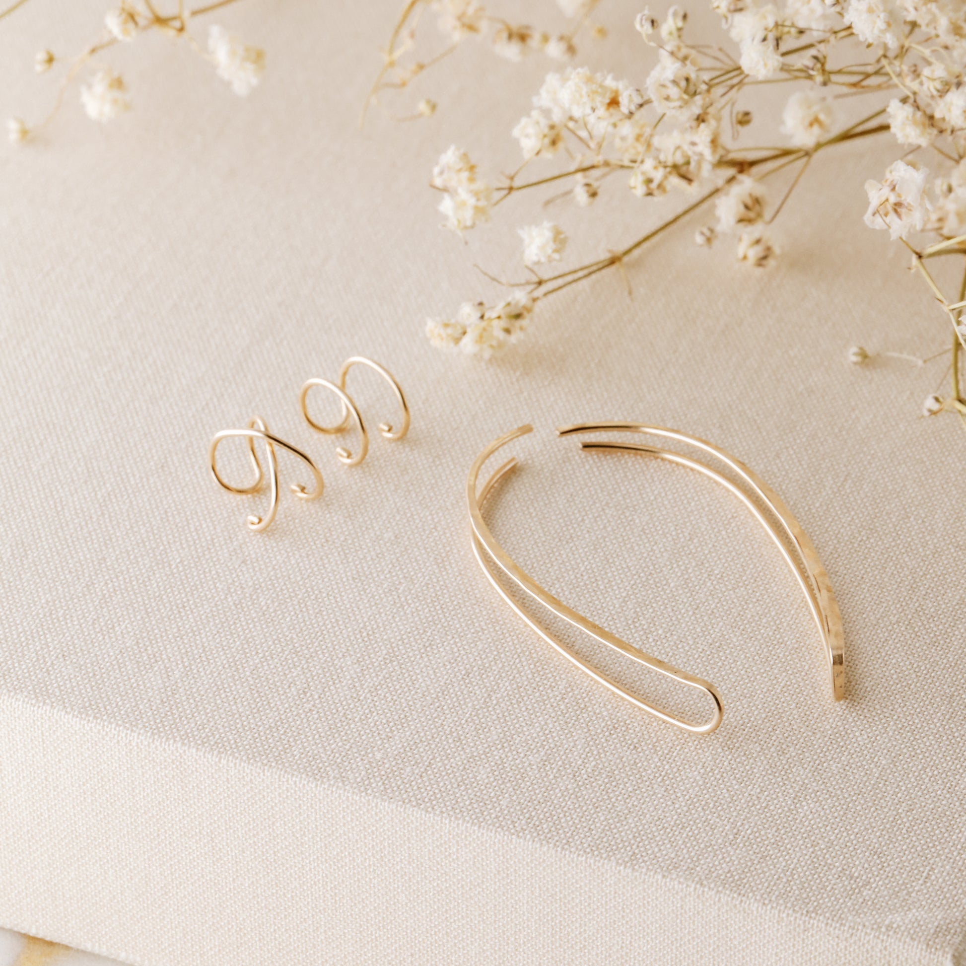 4 pieces ear climber set displayed on beige fabric with dried white flowers, featuring a pair of long hammered ear climbers, one Double Line no-piercing helix cuff and one Criss-Cross no-piercing helix cuff in a warm gold finish.