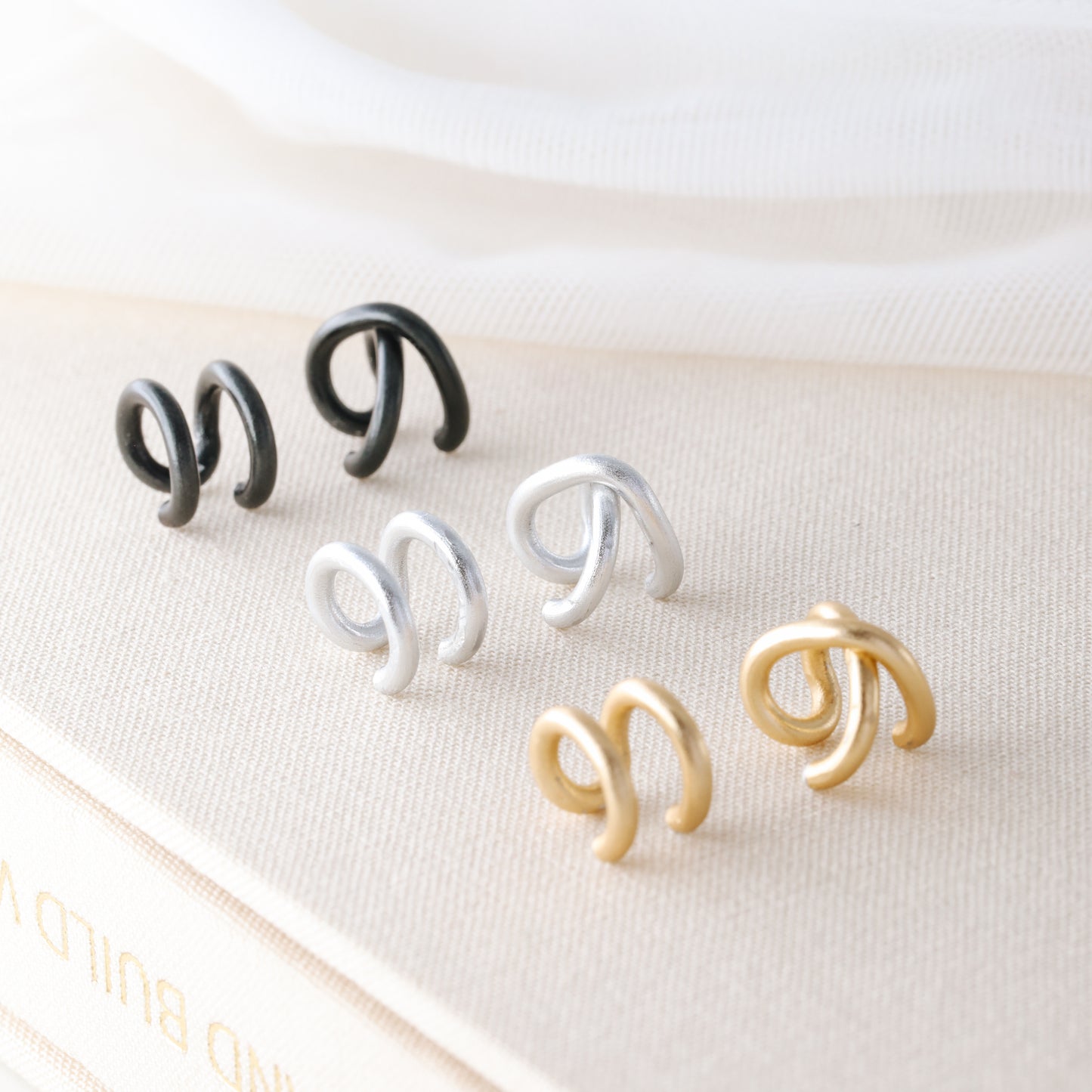 Adjustable no-piercing helix ear cuff shown worn on the upper cartilage area, available in silver, black and soft gold with Double Line and Criss-Cross style options for a bold stacked ear look.