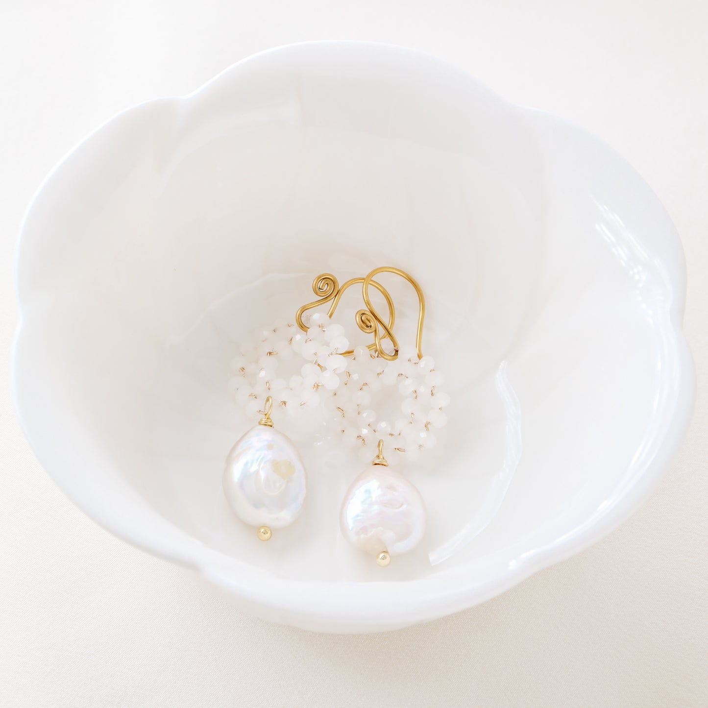 Stainless steel baroque pearl and white crystal wreath drop earrings presented inside a minimalist white ceramic flower-shaped bowl.