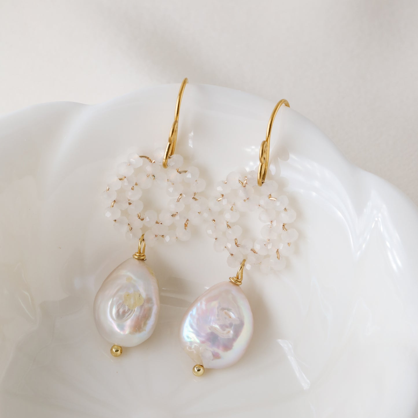 Stainless steel baroque pearl and white crystal wreath drop earrings presented inside a minimalist white ceramic flower-shaped bowl.