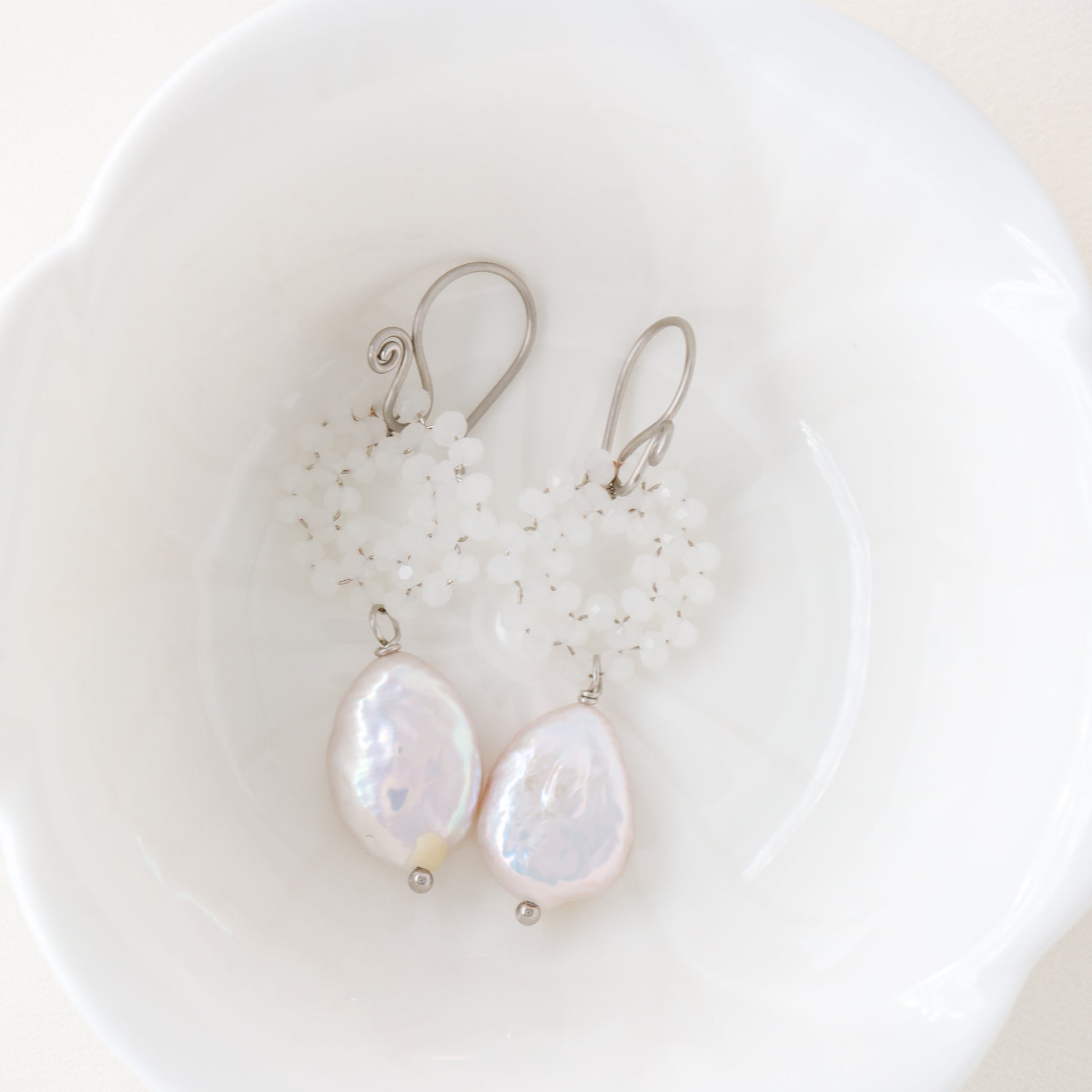 Stainless steel baroque pearl and white crystal wreath drop earrings presented inside a minimalist white ceramic flower-shaped bowl.