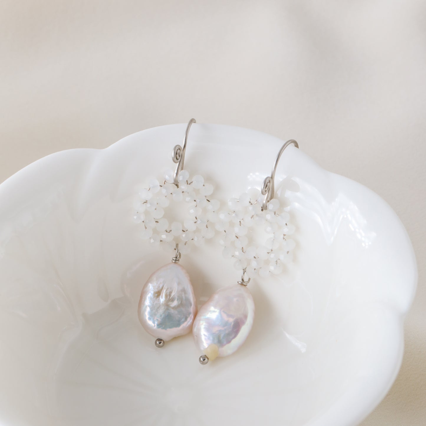 Stainless steel baroque pearl and white crystal wreath drop earrings presented inside a minimalist white ceramic flower-shaped bowl.