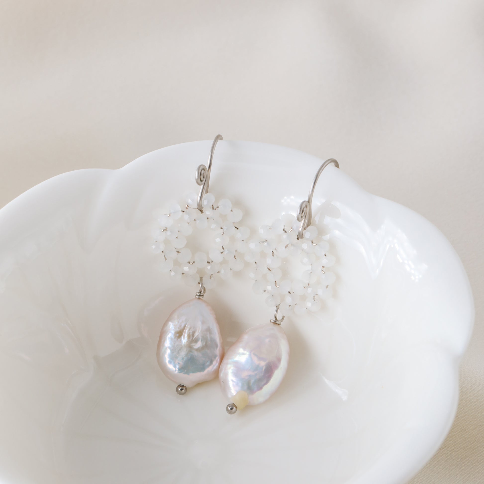 Stainless steel baroque pearl and white crystal wreath drop earrings presented inside a minimalist white ceramic flower-shaped bowl.
