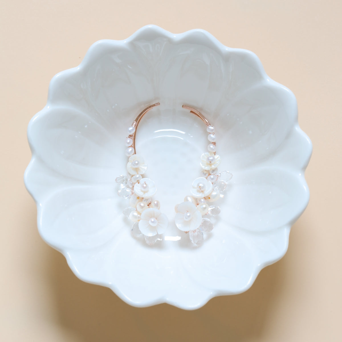Bridal pearl and crystal ear climbers displayed inside a white floral dish, showing the 50 mm curved silhouette, mother-of-pearl blossoms and sparkling crystal details.