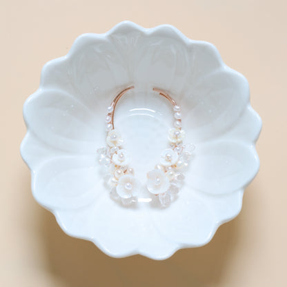 Bridal pearl and crystal ear climbers displayed inside a white floral dish, showing the 50 mm curved silhouette, mother-of-pearl blossoms and sparkling crystal details.