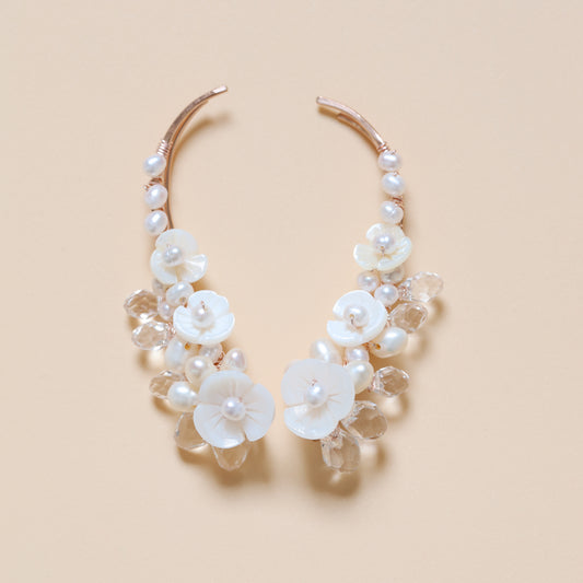 Close-up of matching bridal ear climbers decorated with AA+ freshwater pearls, carved mother-of-pearl flowers and transparent faceted crystal drops, showing the coordinated left and right design.