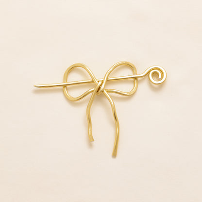 Handmade aluminum bow shawl pin brooch with matching removable stick pin, shown in gold and available in silver or gold finish, designed as a decorative and functional scarf fastener for shawls, sweaters, cardigans, knit wraps and crochet pieces, with a romantic bow shape and minimalist metal design.