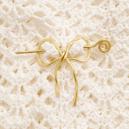 Handmade aluminum bow shawl pin brooch with matching removable stick pin, shown in gold and available in silver or gold finish, designed as a decorative and functional scarf fastener for shawls, sweaters, cardigans, knit wraps and crochet pieces, with a romantic bow shape and minimalist metal design.