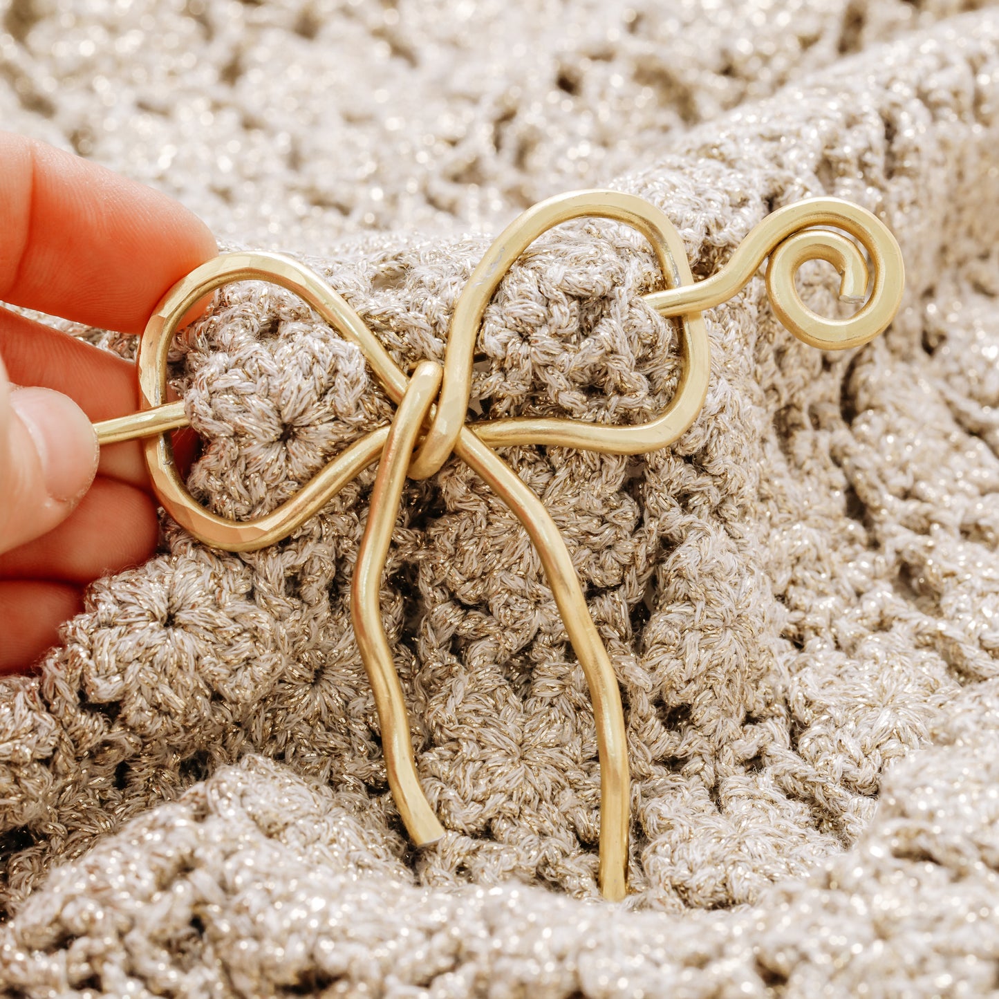 Handmade aluminum bow shawl pin brooch with matching removable stick pin, shown in gold and available in silver or gold finish, designed as a decorative and functional scarf fastener for shawls, sweaters, cardigans, knit wraps and crochet pieces, with a romantic bow shape and minimalist metal design.