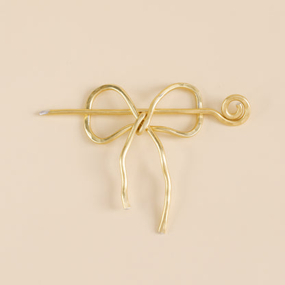 Handmade aluminum bow shawl pin brooch with matching removable stick pin, shown in gold and available in silver or gold finish, designed as a decorative and functional scarf fastener for shawls, sweaters, cardigans, knit wraps and crochet pieces, with a romantic bow shape and minimalist metal design.