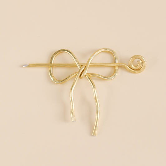 Handmade aluminum bow shawl pin brooch with matching removable stick pin, shown in gold and available in silver or gold finish, designed as a decorative and functional scarf fastener for shawls, sweaters, cardigans, knit wraps and crochet pieces, with a romantic bow shape and minimalist metal design.