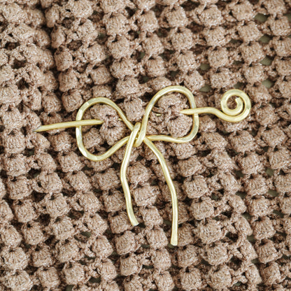 Handmade aluminum bow shawl pin brooch with matching removable stick pin, shown in gold and available in silver or gold finish, designed as a decorative and functional scarf fastener for shawls, sweaters, cardigans, knit wraps and crochet pieces, with a romantic bow shape and minimalist metal design.