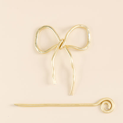 Handmade aluminum bow shawl pin brooch with matching removable stick pin, shown in gold and available in silver or gold finish, designed as a decorative and functional scarf fastener for shawls, sweaters, cardigans, knit wraps and crochet pieces, with a romantic bow shape and minimalist metal design.