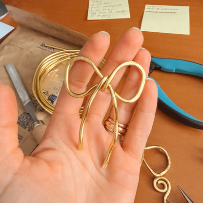 Handmade aluminum bow shawl pin brooch with matching removable stick pin, shown in gold and available in silver or gold finish, designed as a decorative and functional scarf fastener for shawls, sweaters, cardigans, knit wraps and crochet pieces, with a romantic bow shape and minimalist metal design.