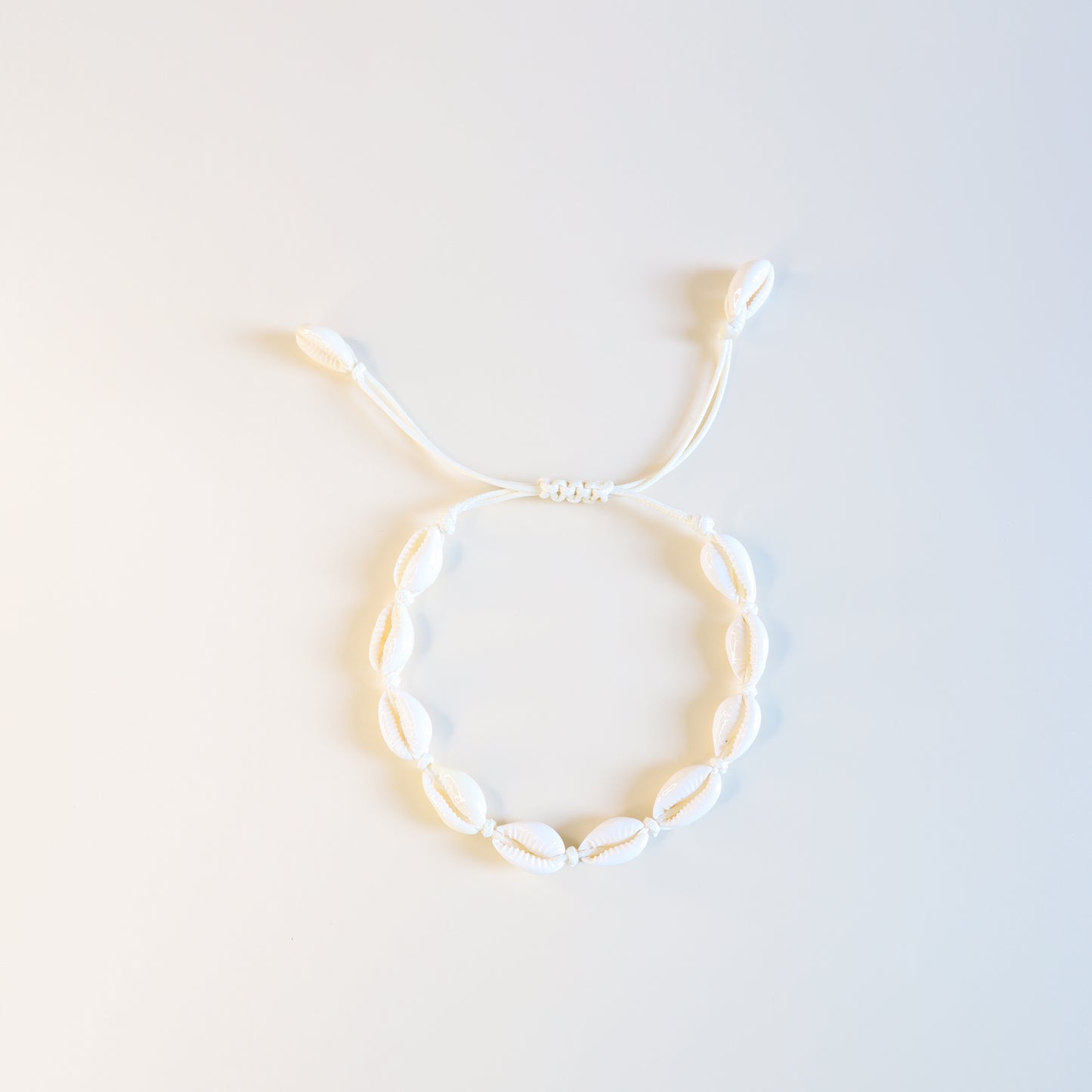 Close up of cream cotton cord anklet with natural cowrie shells and sliding knot closure