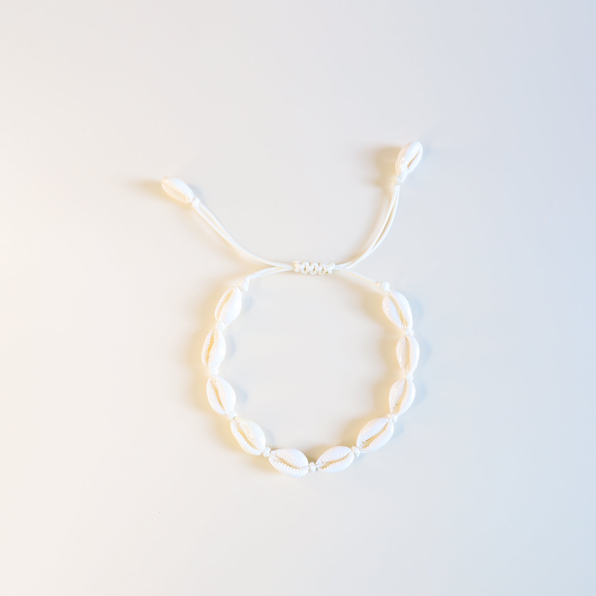 Close up of cream cotton cord anklet with natural cowrie shells and sliding knot closure