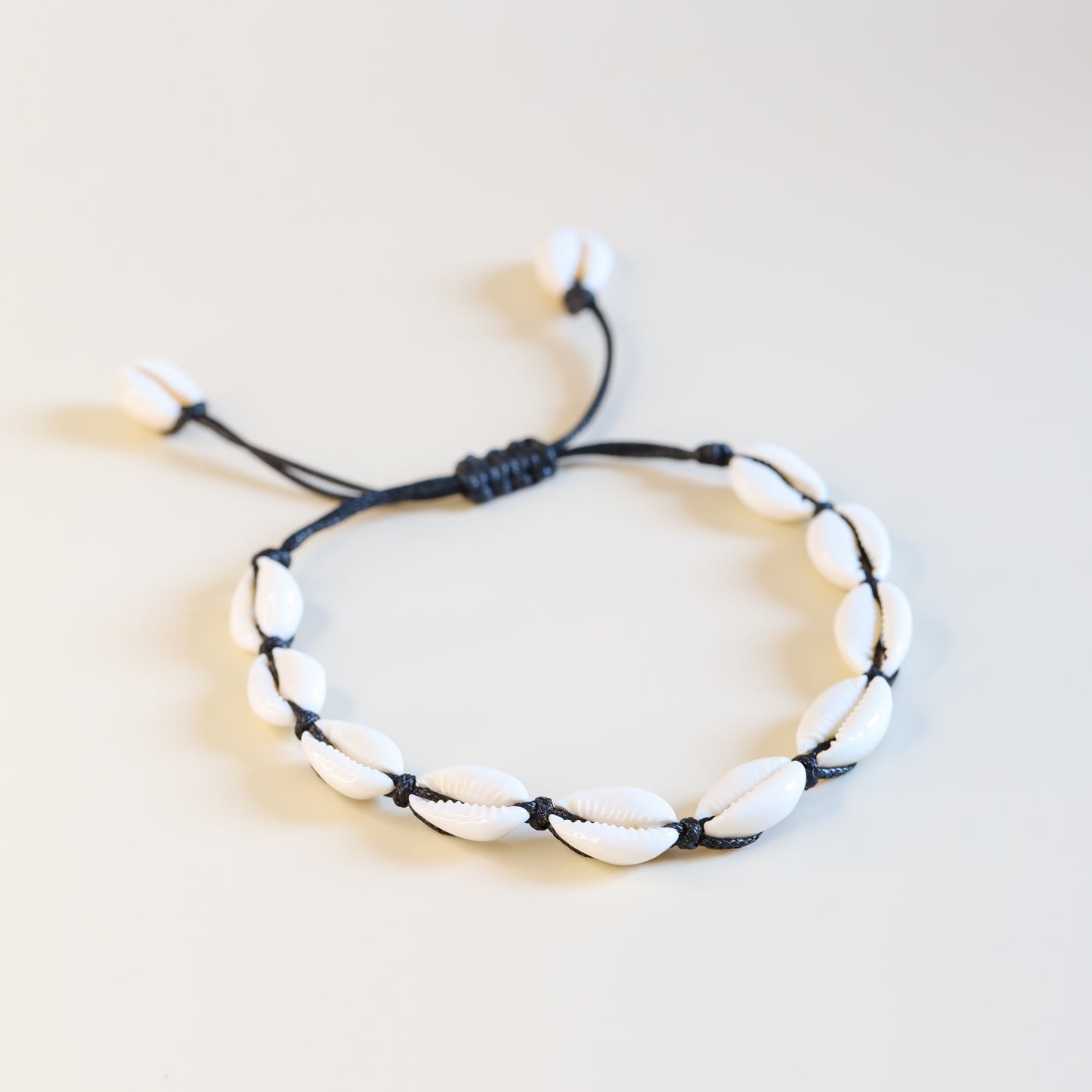 Cowrie shell anklet with black cotton cord worn on ankle at the beach