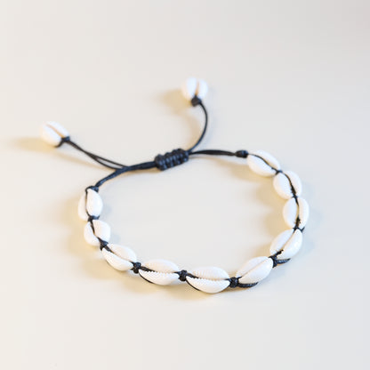 Cowrie shell anklet with black cotton cord worn on ankle at the beach