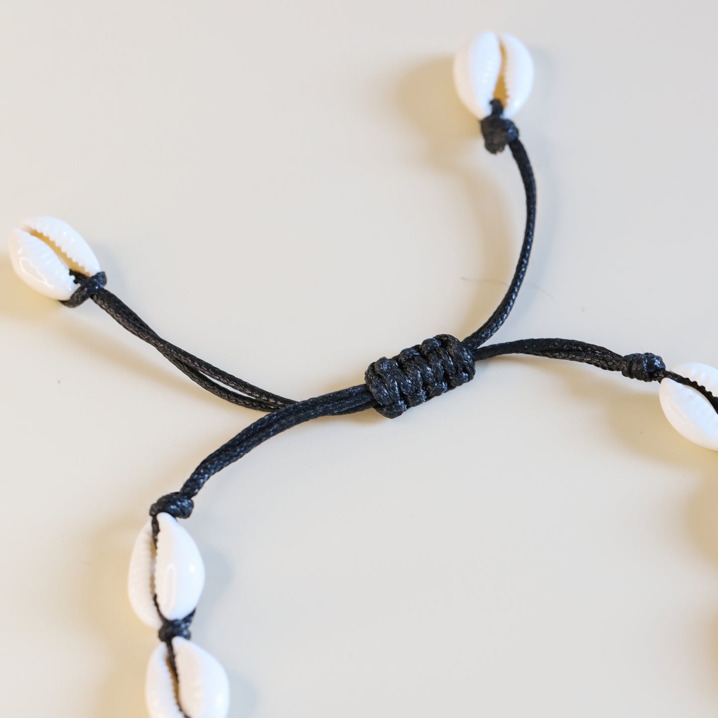 Cowrie shell anklet with black cotton cord worn on ankle at the beach