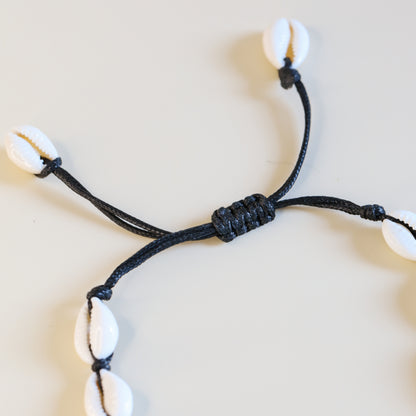 Cowrie shell anklet with black cotton cord worn on ankle at the beach
