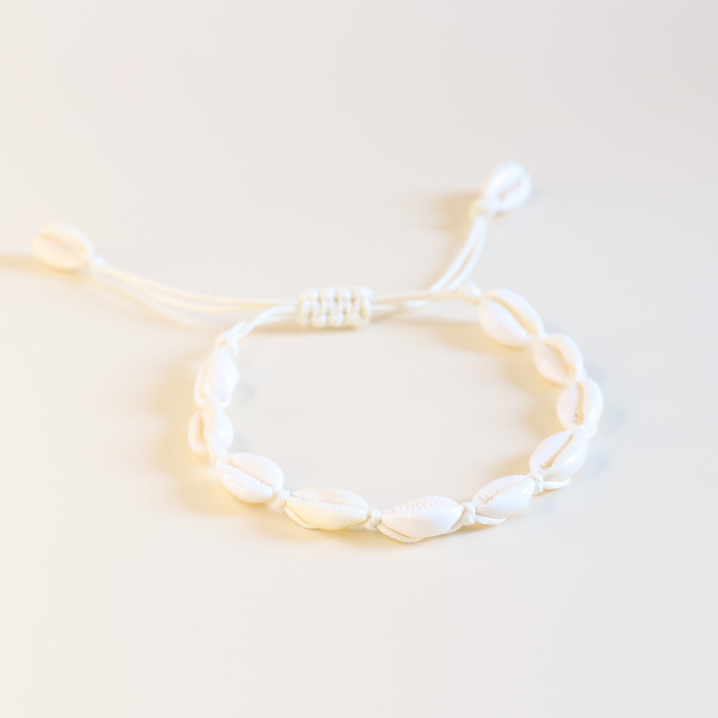 Close up of cream cotton cord anklet with natural cowrie shells and sliding knot closure