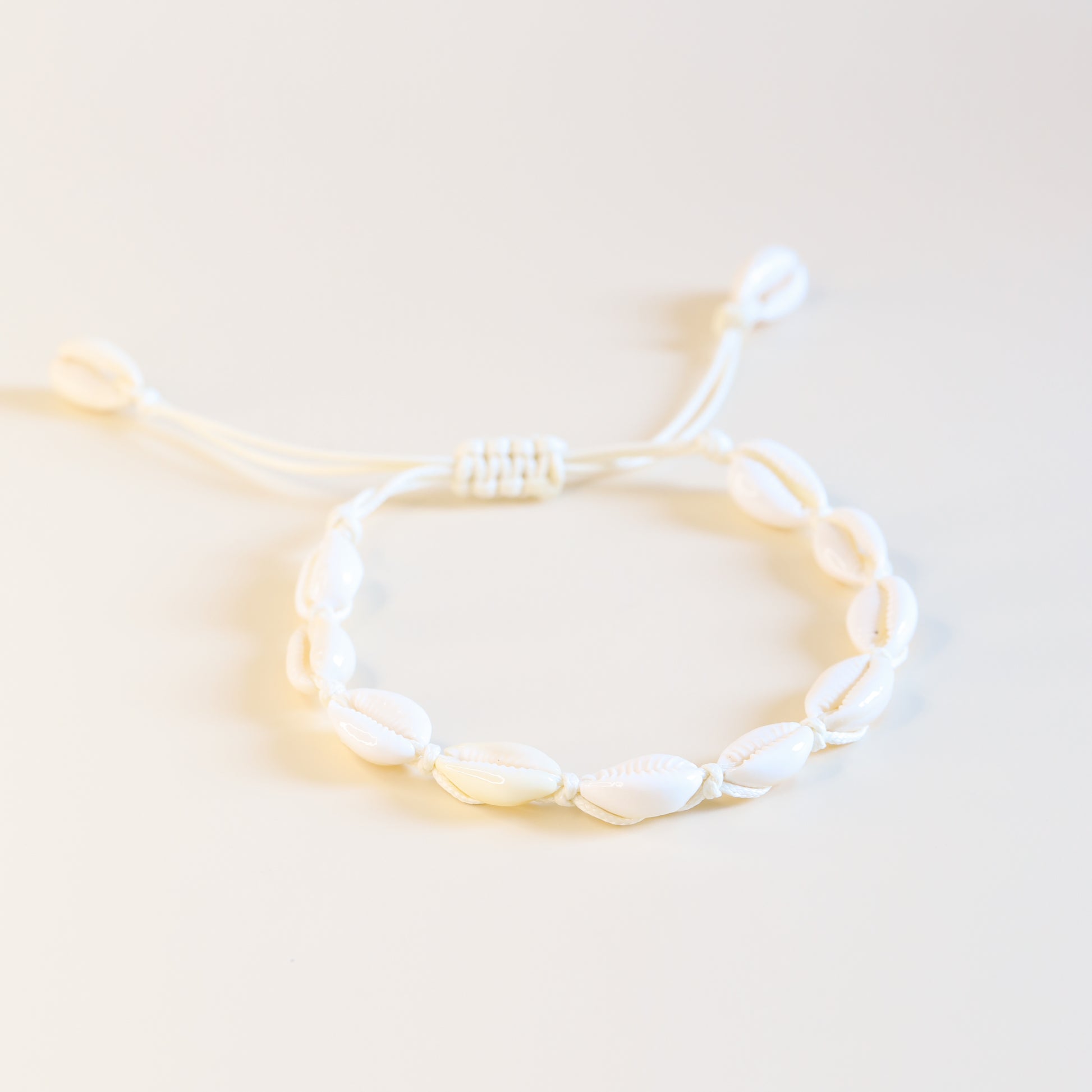 Close up of cream cotton cord anklet with natural cowrie shells and sliding knot closure