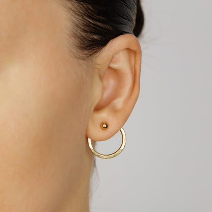Gold hammered round ear jacket worn behind the earlobe with a polished ball stud, creating the appearance of a hoop suspended beneath the stud.