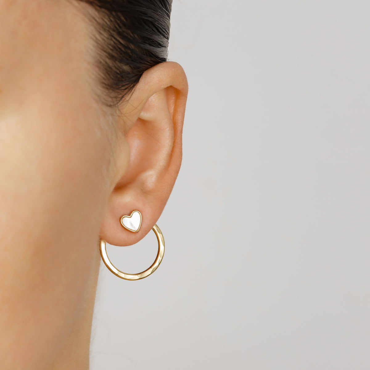 Gold round ear jacket worn with a white heart stud at the front, demonstrating how the same jacket can be styled with different stud designs.