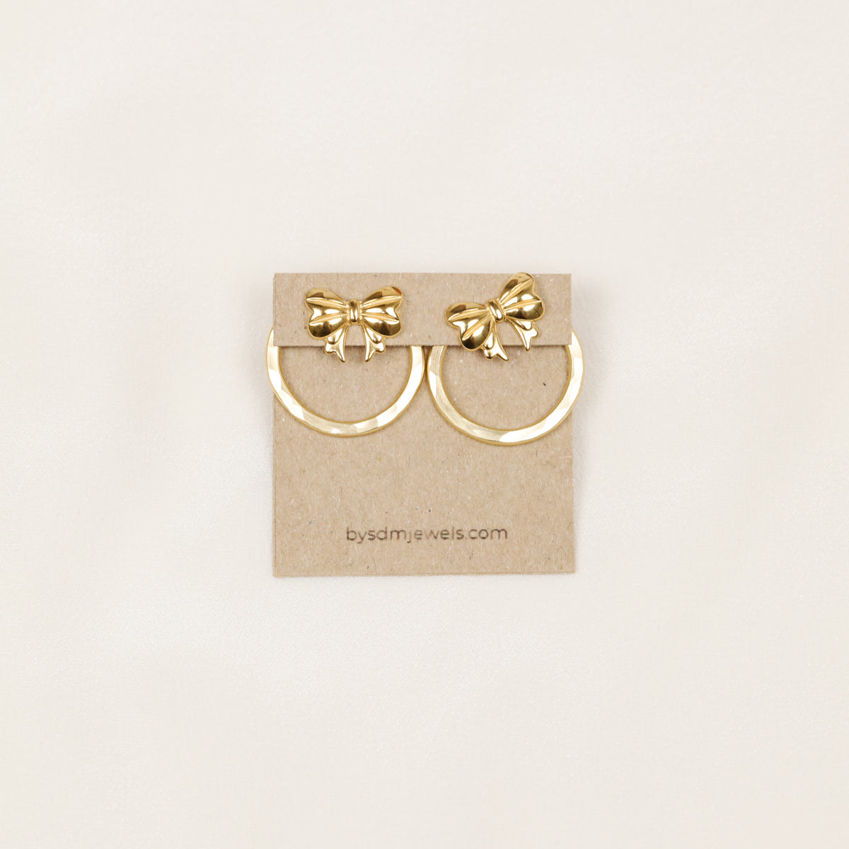 Pair of gold hammered round ear jackets displayed with decorative bow studs for a playful interchangeable earring combination.