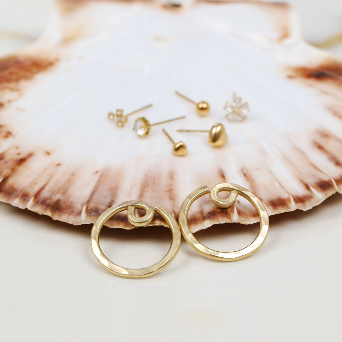 Two handmade gold circular ear jacket backs displayed with assorted stud earrings, illustrating the interchangeable mix and match concept.