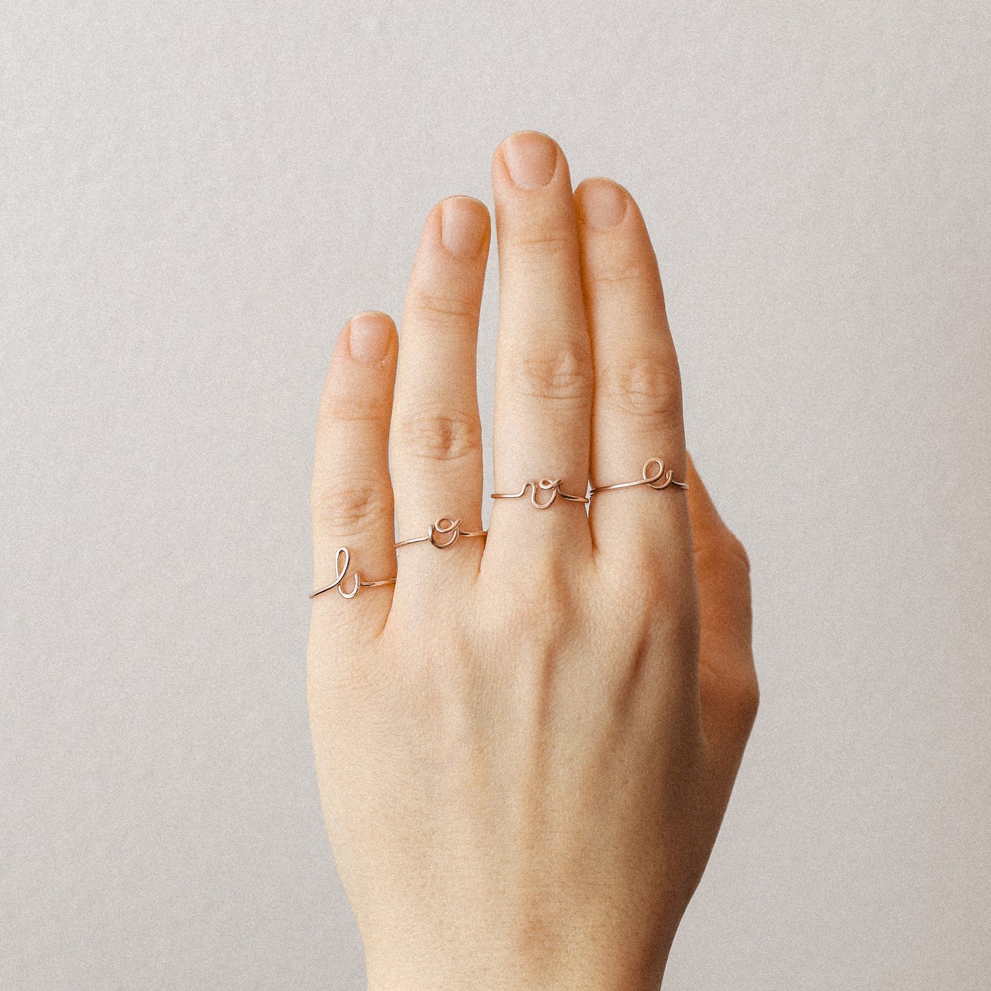 Close-up of a handmade 14k rose gold filled wire ring shaped into the letter L, O, V and E on a woman's fingers.