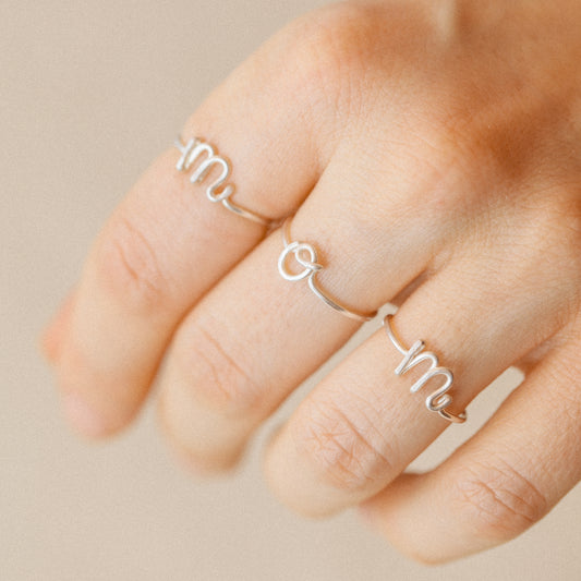 Close-up of a handmade 925 sterling silver wire ring shaped into the letter M, O and M on a woman's fingers.