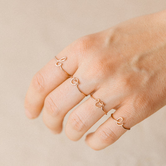 Close-up of a handmade 14k rose gold filled wire ring shaped into the letter L, O, V and E on a woman's fingers.