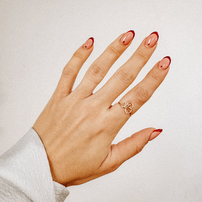 Handmade gold wire ring featuring an uppercase cursive letter B, styled on a hand with a red French manicure.