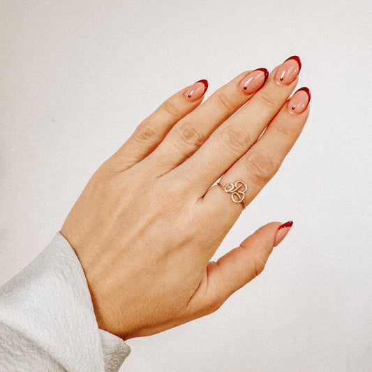 Close-up of a handmade gold wire ring with an uppercase cursive letter B design, worn on a hand.