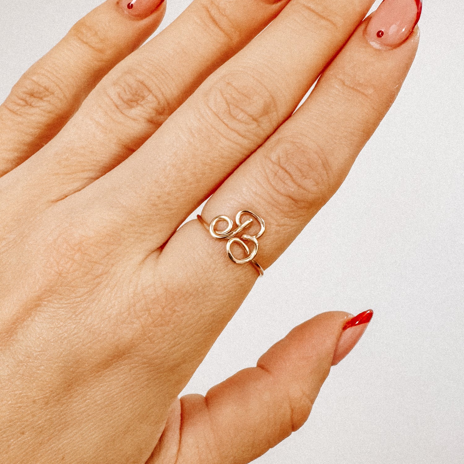 Close-up of a handmade gold wire ring with an uppercase cursive letter B design, worn on a hand.