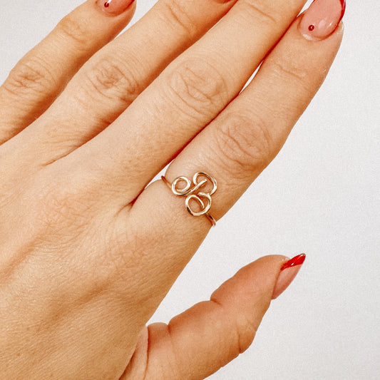 Close-up of a handmade gold wire ring with an uppercase cursive letter B design, worn on a hand.