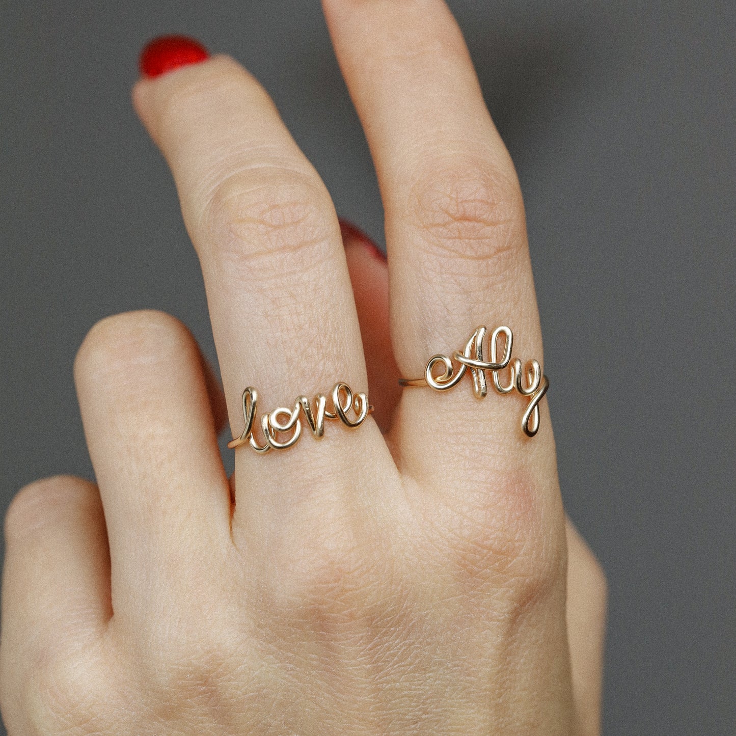 Two custom gold wire name rings featuring "Aly" and "Love" worn together for a stacking effect.