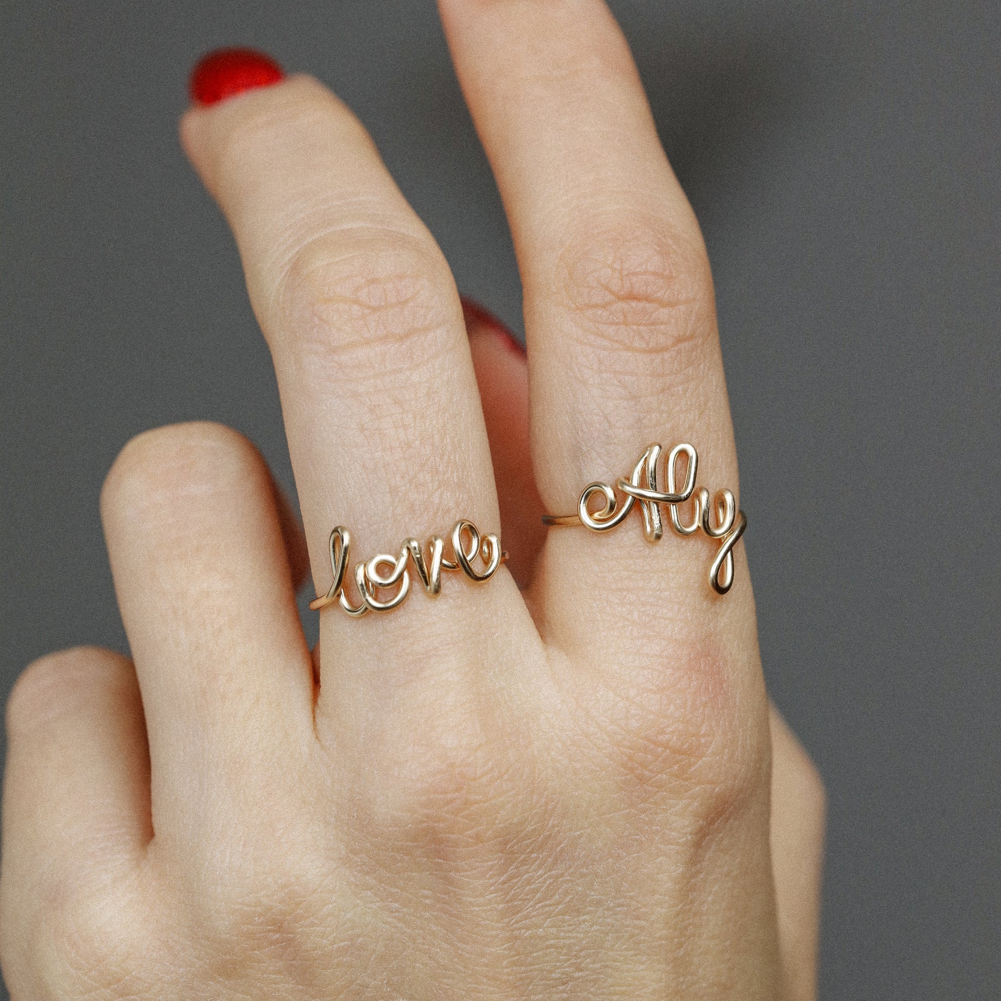 Two custom gold wire name rings featuring "Aly" and "Love" worn together for a stacking effect.
