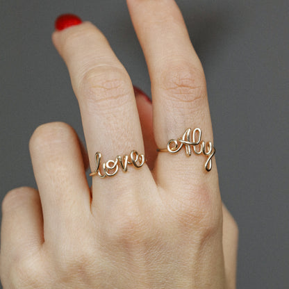 Two custom gold wire name rings featuring "Aly" and "Love" worn together for a stacking effect.