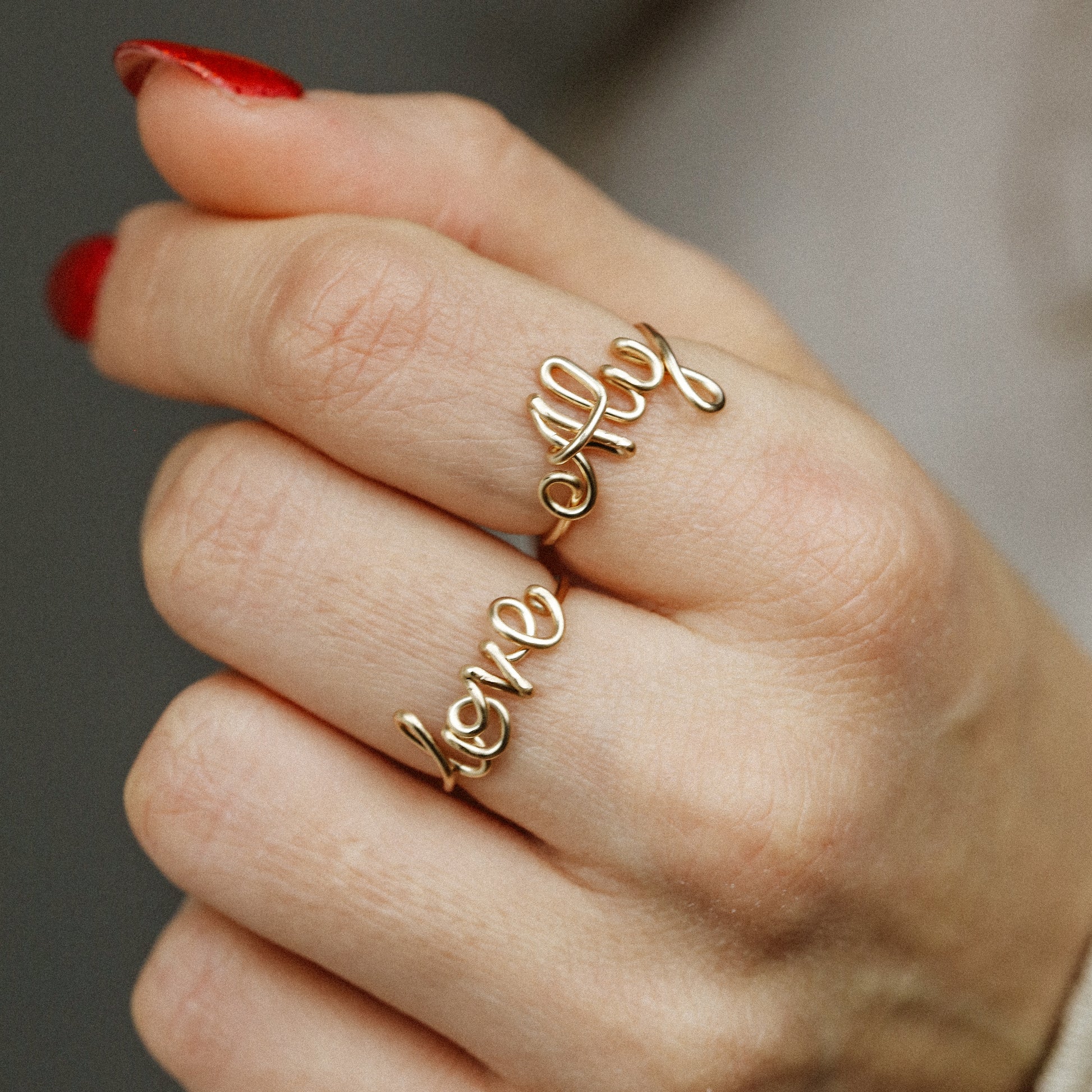 Two custom gold wire name rings featuring "Aly" and "Love" worn together for a stacking effect.