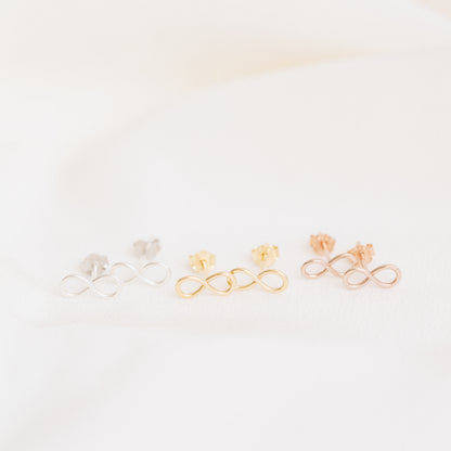 Tiny infinity stud earrings in silver gold and rose gold on soft white fabric