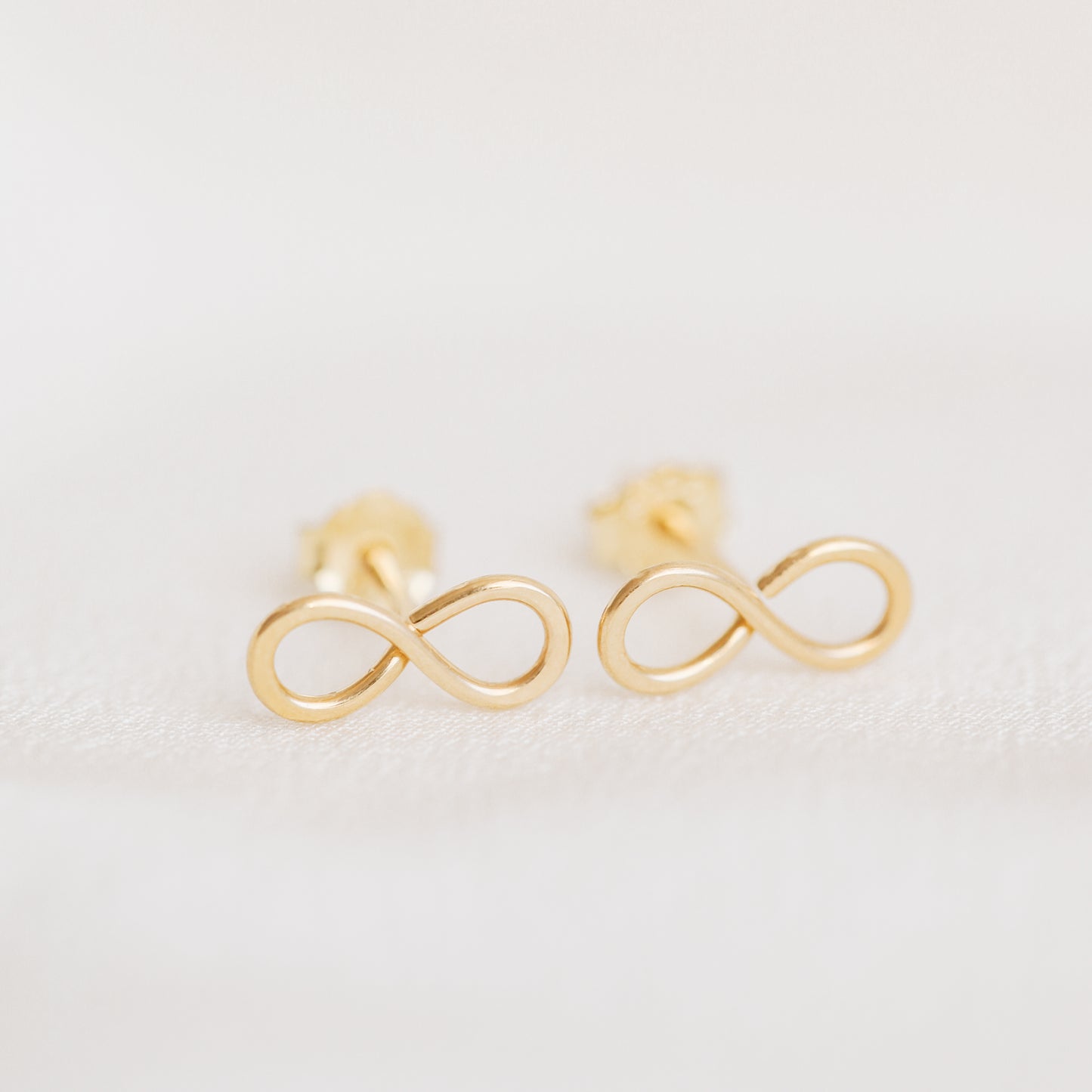 Minimal gold infinity symbol stud earrings close up on white background